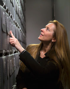 Allison McGourty touches index finger to a tall metal wall of music archives, looking upward