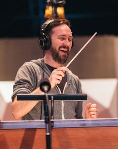 Composer Jeremy Turner conducting with baton and a big smile