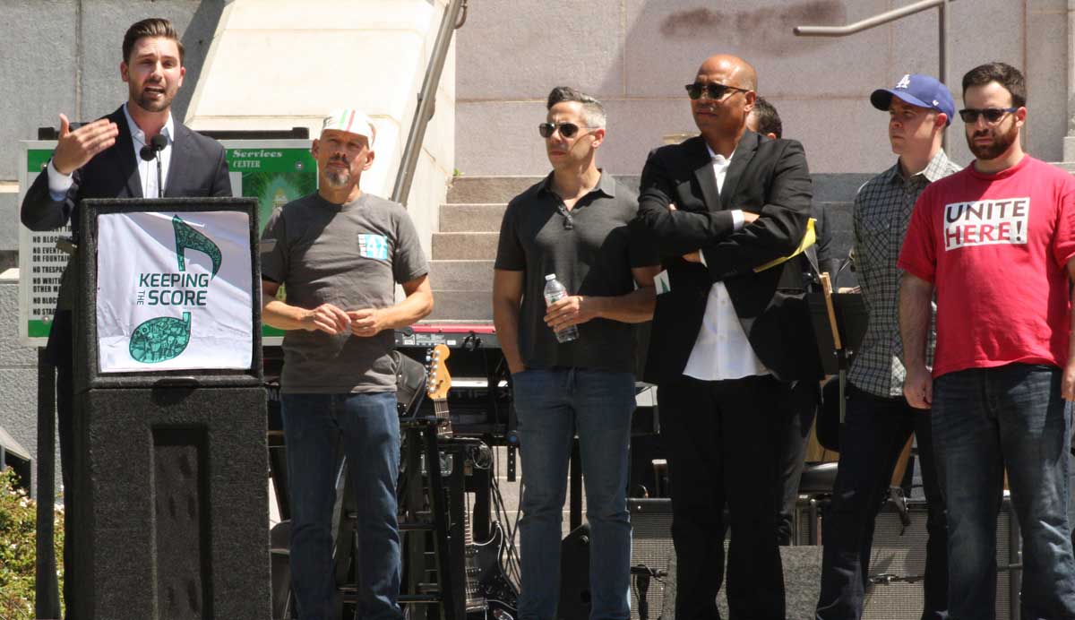 Ian Calderon and associates address crowd on stairs of Los Angeles City Hall.