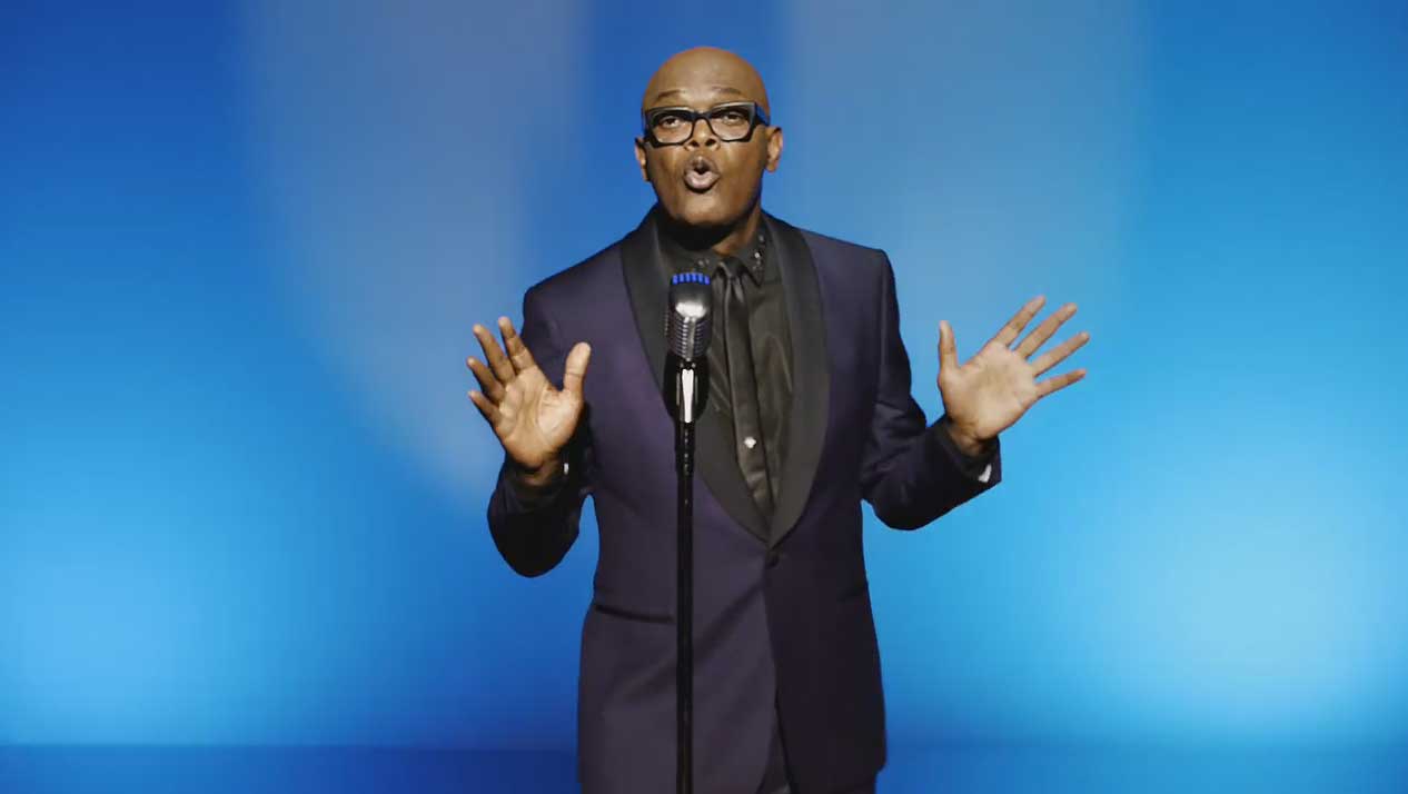 Samuel L. Jackson looks suave in black-on-black suit, singing with hands raised at microphone