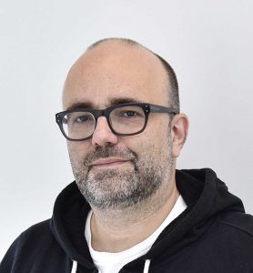 Composer Alex Geringas poses in glasses and a hoodie