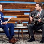 Chris Isaacs strums a guitar as Dave Karger shuffles papers.