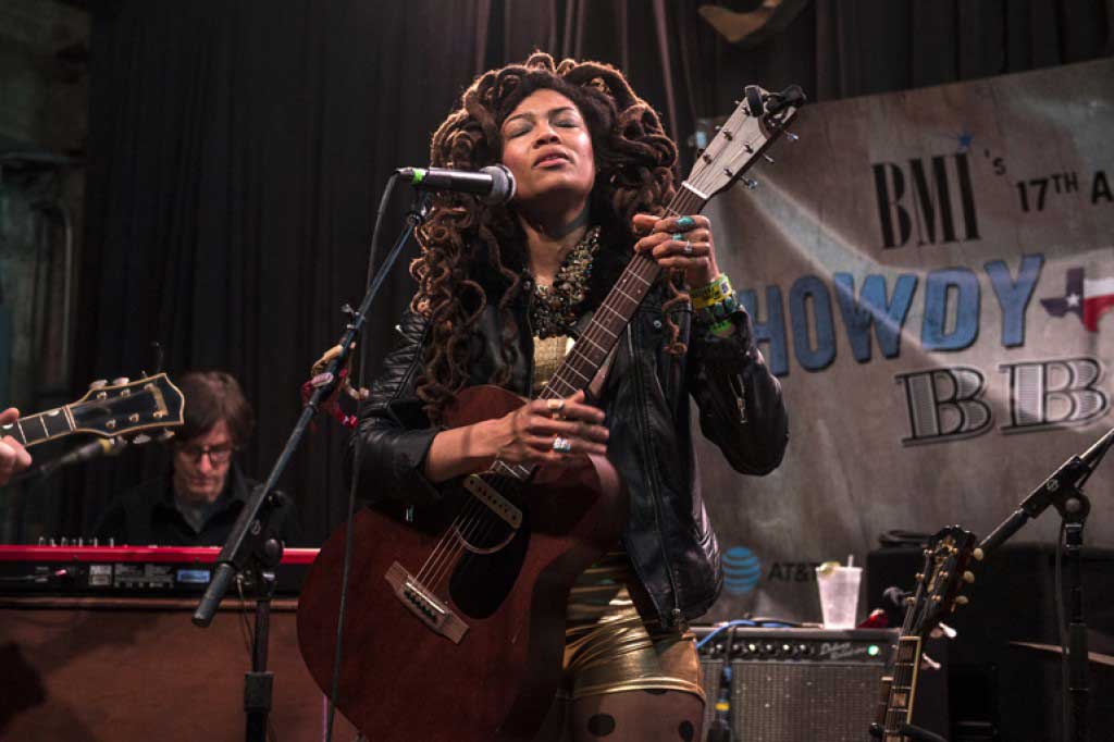 Valerie June at microphone with acoustic guitar.