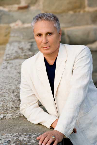 John Corigliano poses in a white jacket and black shirt.